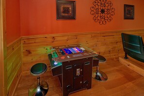 A room with a wooden bench, a table with a video game console, two stools, and a television on the right. - Almost Heaven Cabin Rental (Pigeon Forge)