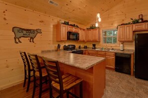 A kitchen with wooden cabinets, a granite countertop, a microwave, a stove, and a refrigerator. - Almost Paradise Cabin Rental (Pigeon Forge)