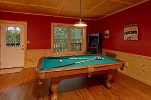 A pool table with balls, a window with a view of trees, a Coca-Cola sign, and a poster on the wall. - Almost Paradise Cabin Rental (Pigeon Forge)
