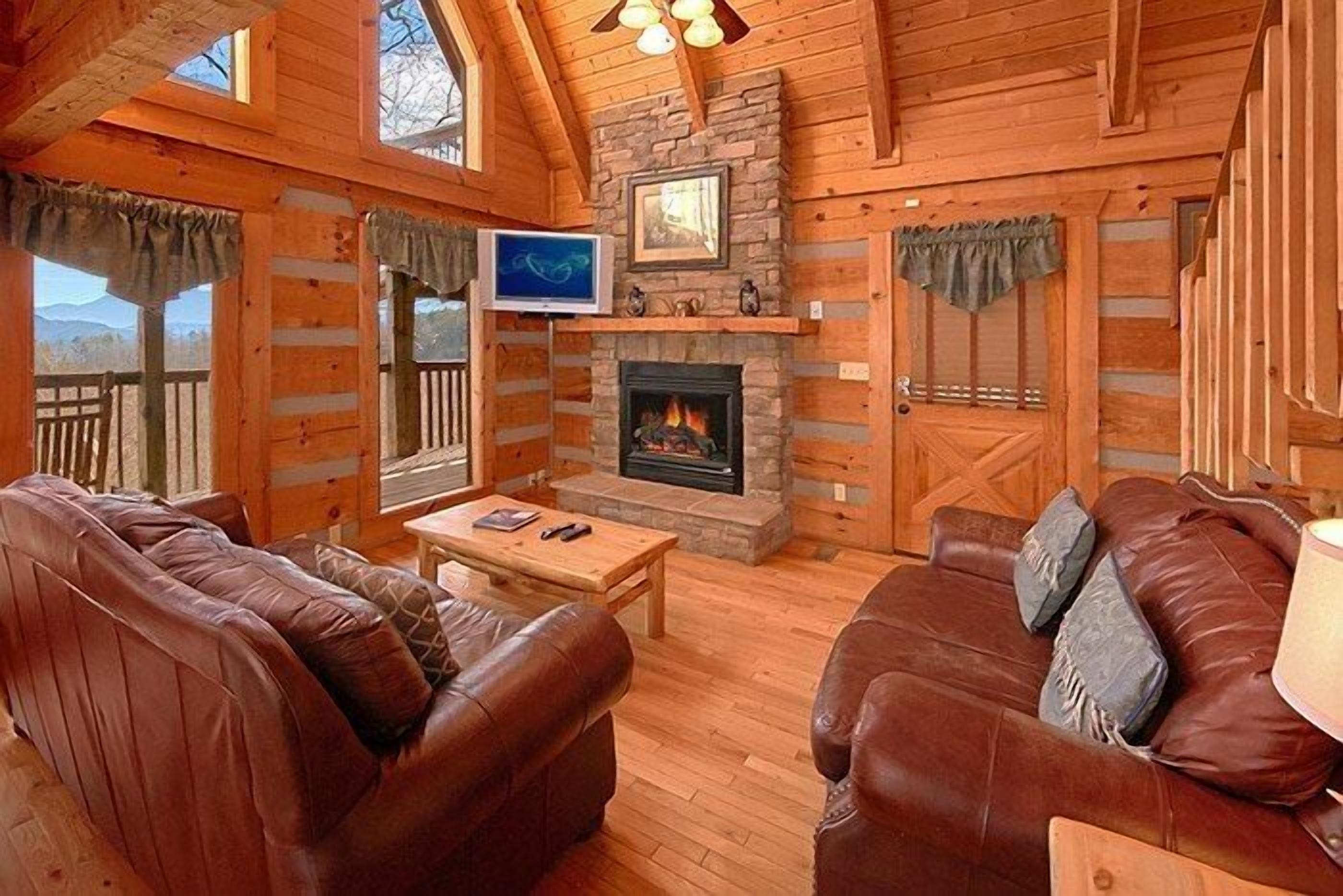 A log cabin interior with a fireplace, leather sofas, a television, and a wooden ceiling.