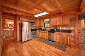 A wooden cabin interior with a kitchen featuring a refrigerator, stove, microwave, and wooden cabinets. - Altitude Adjustment Cabin Rental (Wears Valley)