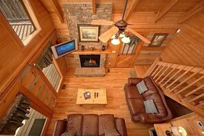 A log cabin interior with a fireplace, wooden furniture, a television, and a ceiling fan. - Altitude Adjustment Cabin Rental (Wears Valley)