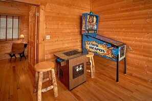 A wooden interior with a vintage arcade machine, a wooden stool, and a small table. - Altitude Adjustment Cabin Rental (Wears Valley)