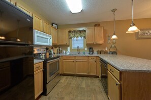 A kitchen with wooden cabinets, a stainless steel refrigerator, a microwave, and a sink. - Amazing Grace II Vacation Home (Pigeon Forge)