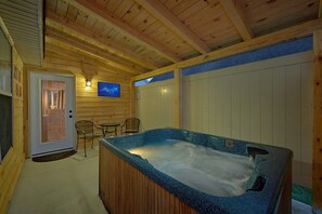 A wooden cabin interior with a hot tub, two chairs, a television, and a door leading to an outdoor area. - Amazing Grace II Vacation Home (Pigeon Forge)