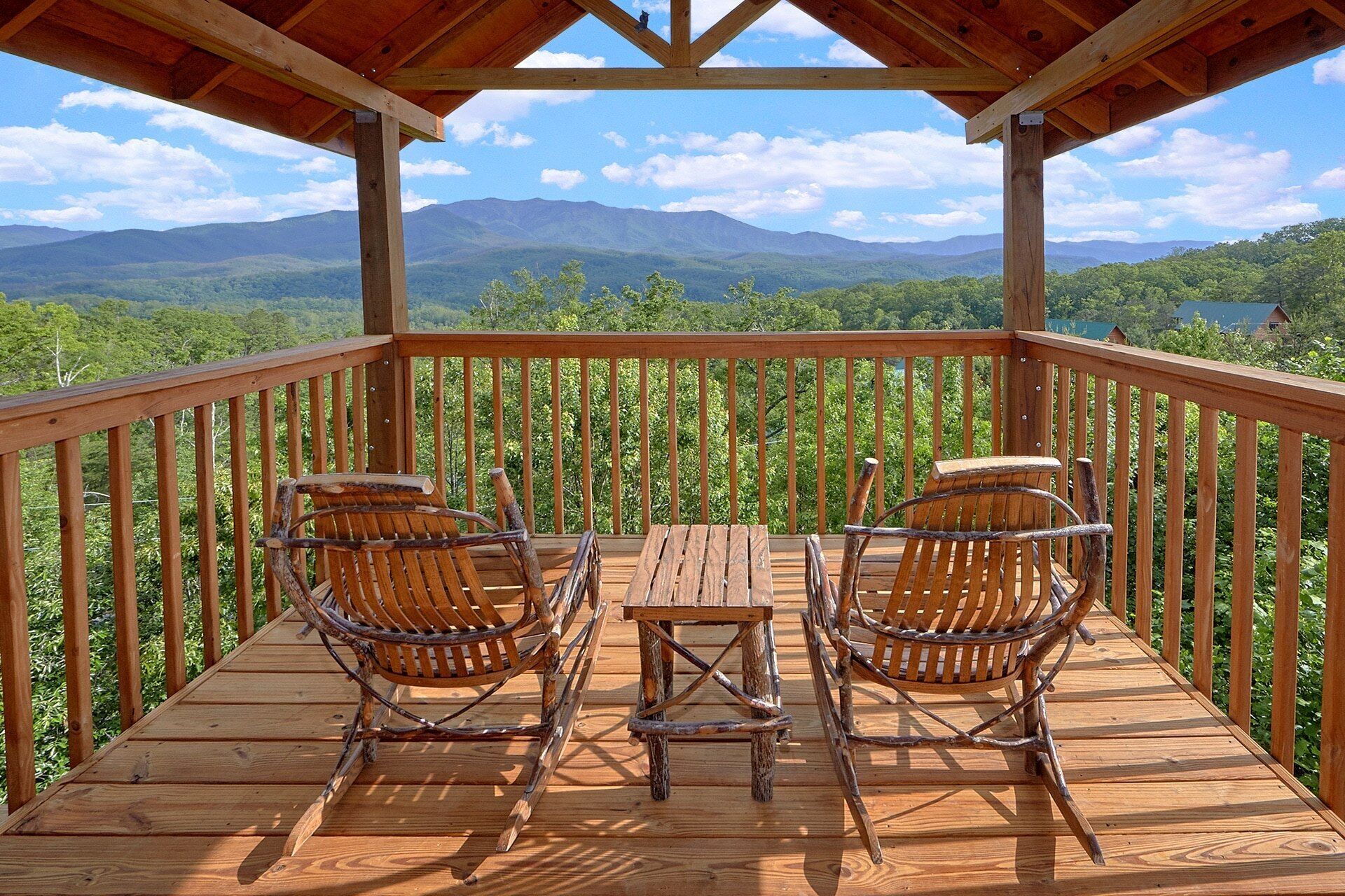 Eine Holzterrasse mit zwei Korbstühlen und einem kleinen Tisch, mit Blick auf eine gebirgige Landschaft.