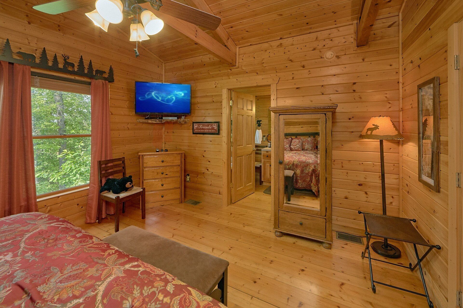 A wooden cabin room with a bed, a television, a dresser, and a mirror.