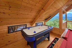 A wooden-floored room with a foosball table and a window overlooking a forested area. - Angel's Landing Cabin Rental (Gatlinburg)