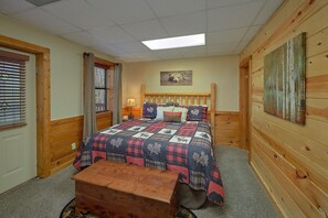 A room with a bed, a wooden bench, a window with blinds, a lamp, and a painting on the wall. - Angel's Ridge Cabin Rental (Pigeon Forge)