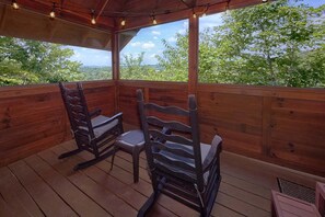 A wooden deck with two rocking chairs and a covered area with string lights. - Angel's Ridge Cabin Rental (Pigeon Forge)