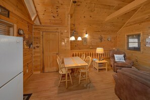 A wooden cabin interior with a dining table, chairs, a sofa, and a refrigerator. - Angel's Ridge Cabin Rental (Pigeon Forge)