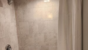 A shower area with a white tiled wall, a showerhead, and a curtain with a floral pattern.