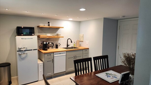 A compact kitchen with a microwave, coffee maker, and a sink. There are cabinets, a dishwasher, and a dining table with chairs.