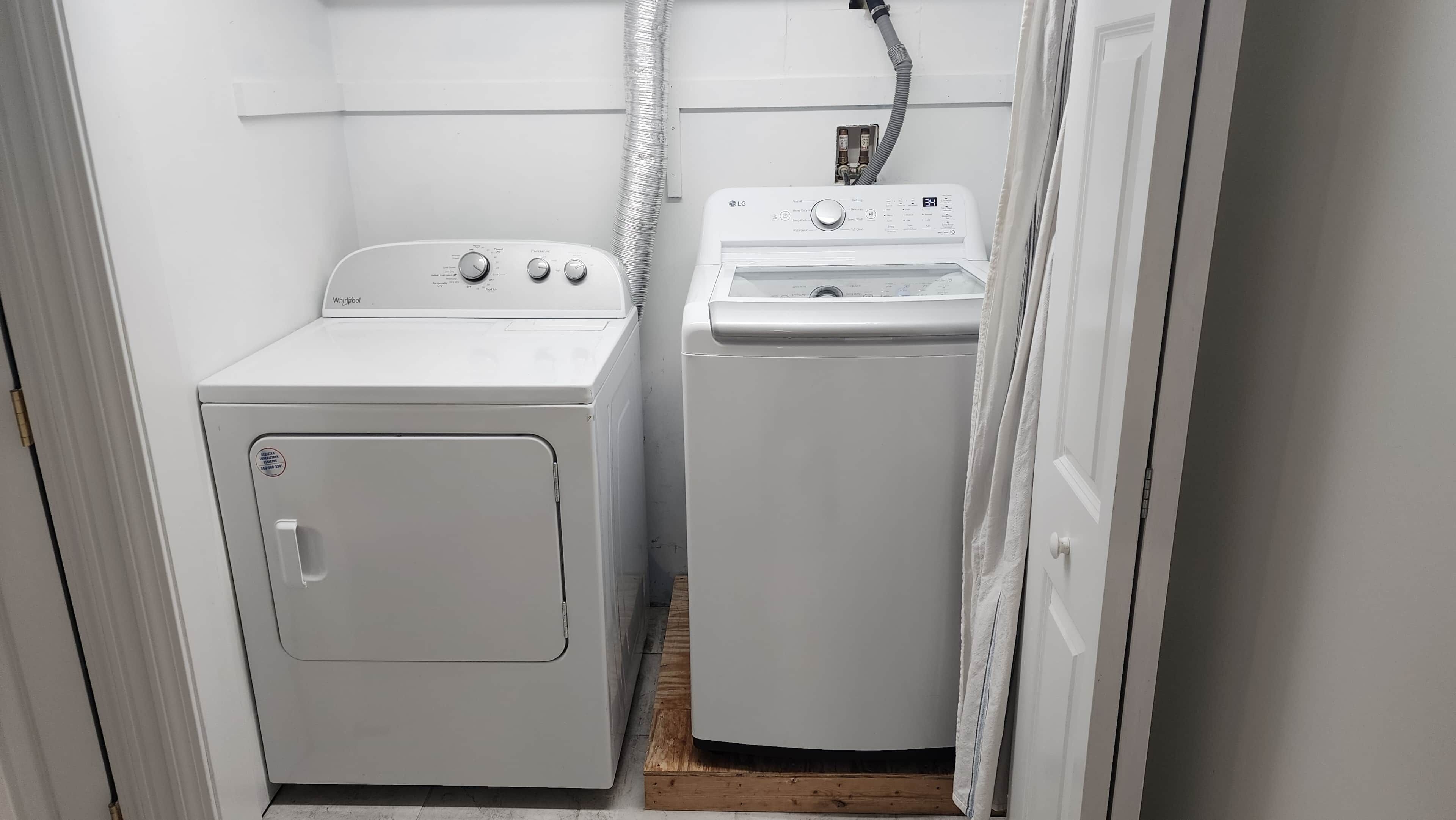 A laundry room with a front-loading washer and dryer, wooden flooring, and a white door.