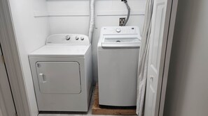 A laundry room with a front-loading washer and dryer, wooden flooring, and a white door.