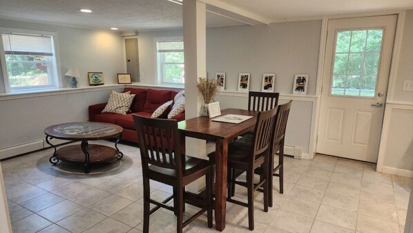 A dining area with a wooden table and chairs, a red sofa, and a small round table with a decorative plate.