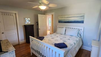 A bedroom with a bed, a ceiling fan, a door, and a painting on the wall.