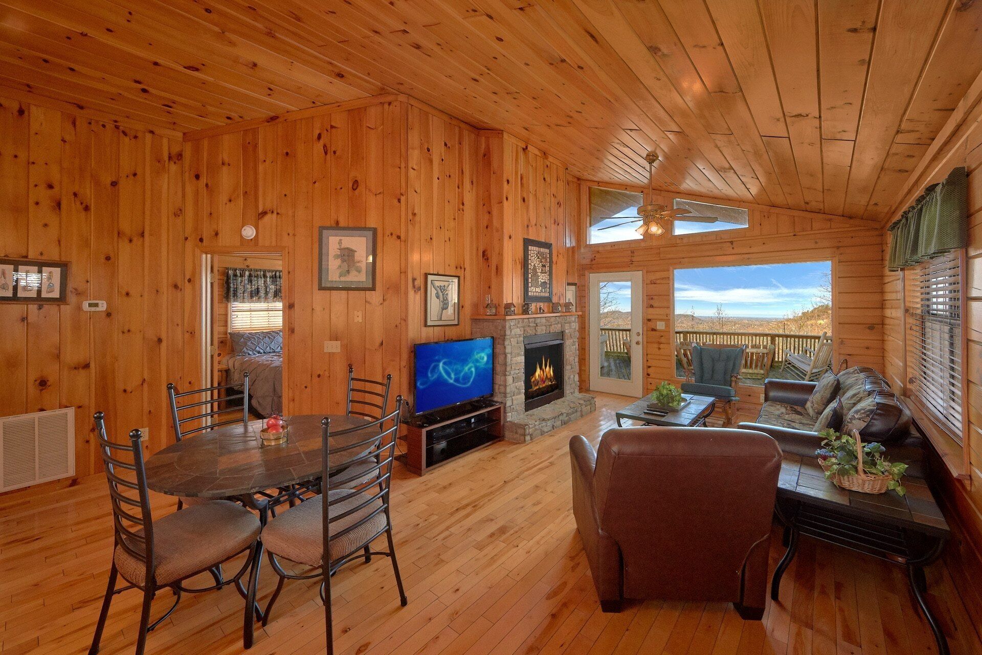 Ein Interieur einer Holzhütte mit Essbereich, Kamin, Fernseher und einer Sitzecke mit Aussicht.