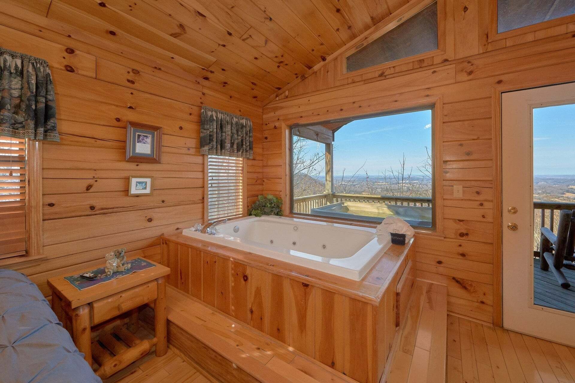 A wooden cabin interior with a hot tub, a bench, and a view of the landscape.
