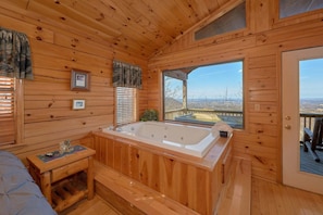Ein Holzblockhaus-Interieur mit Whirlpool, einer Sitzbank und Blick auf die Landschaft.