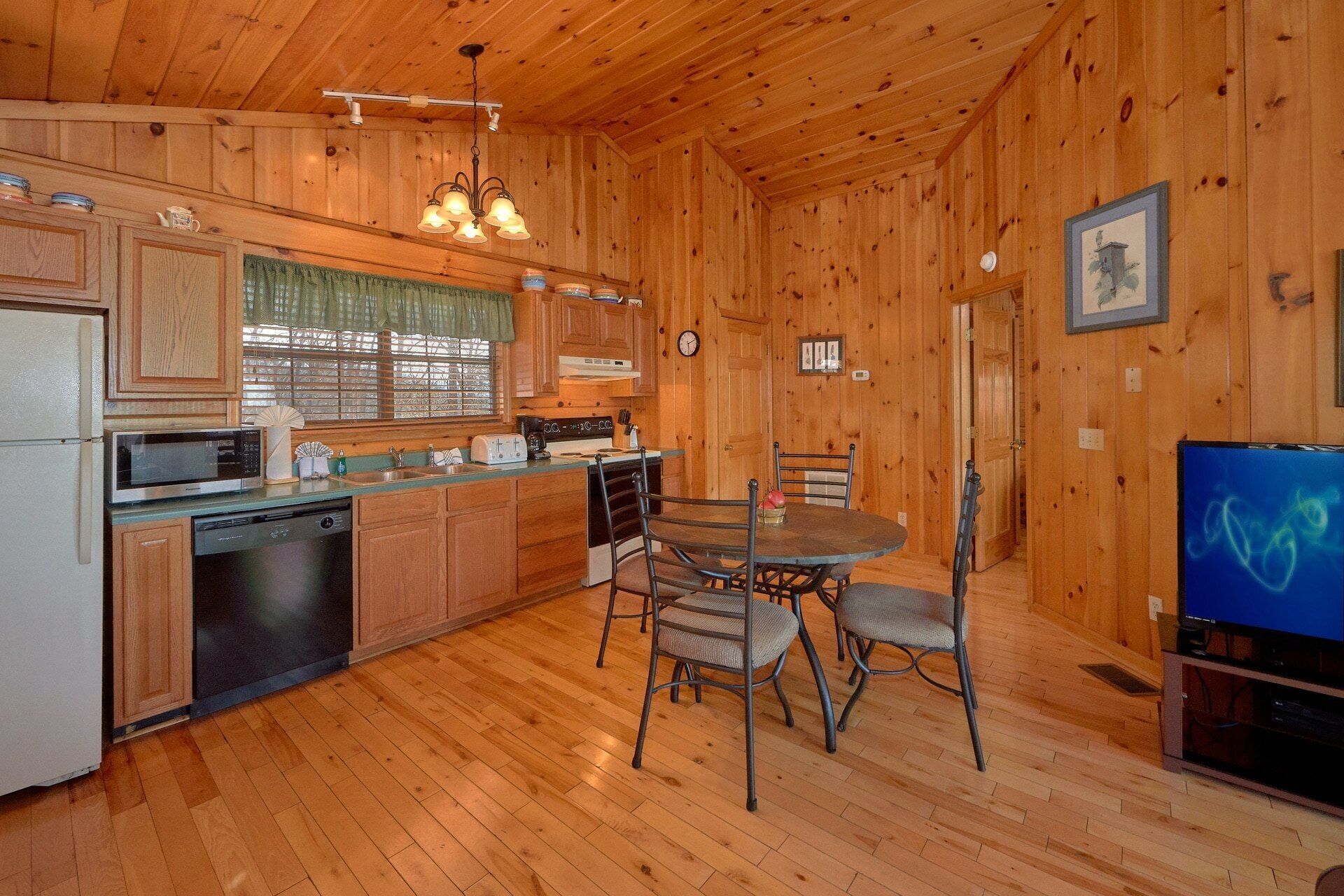 A wooden cabin interior with a kitchen, dining area, and a television.