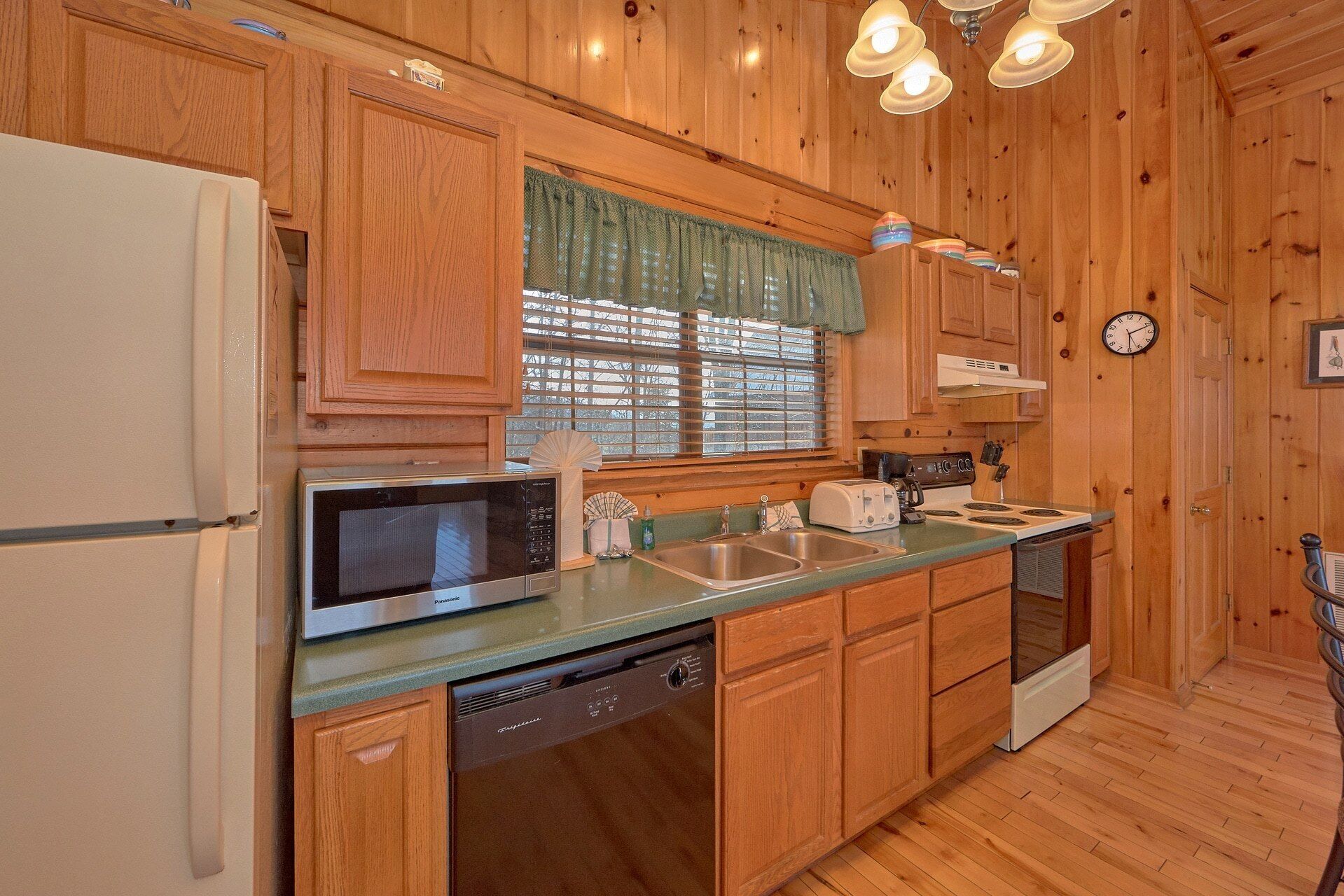 A kitchen with wooden cabinets, a microwave, a dishwasher, a toaster, and a clock on the wall.