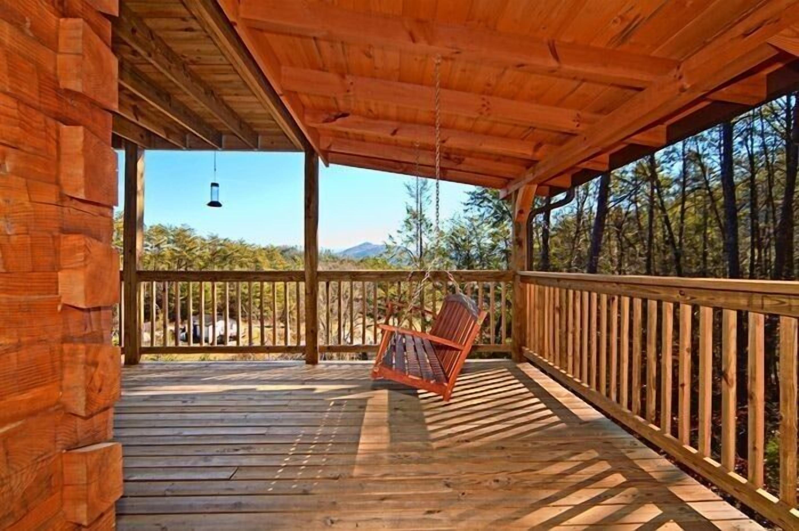 Eine Holzterrasse mit einer Schaukel, einer Hängeleuchte und Blick auf Bäume und Berge.