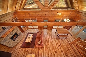 A wooden interior with a stone fireplace, wooden furniture, and a high ceiling with skylights. - Apache Sunset Cabin Rental (Wears Valley)