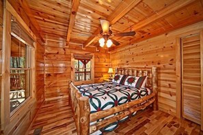 A wooden cabin interior with a bed, a ceiling fan, and a window. - Apache Sunset Cabin Rental (Wears Valley)