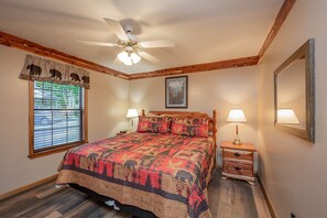 A bedroom with a bed, two bedside lamps, a ceiling fan, a window with blinds, a framed picture on the wall, and a wooden floor. - Appalachian Bear Den Cabin Rental (Pigeon Forge)
