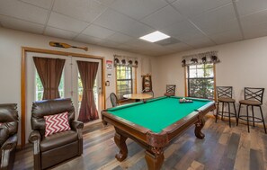 A pool table with surrounding chairs, a wooden paddle, and a bear-themed curtain. - Appalachian Bear Den Cabin Rental (Pigeon Forge)