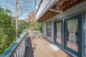 Une terrasse en bois avec une rambarde, une petite table et deux fauteuils à bascule.