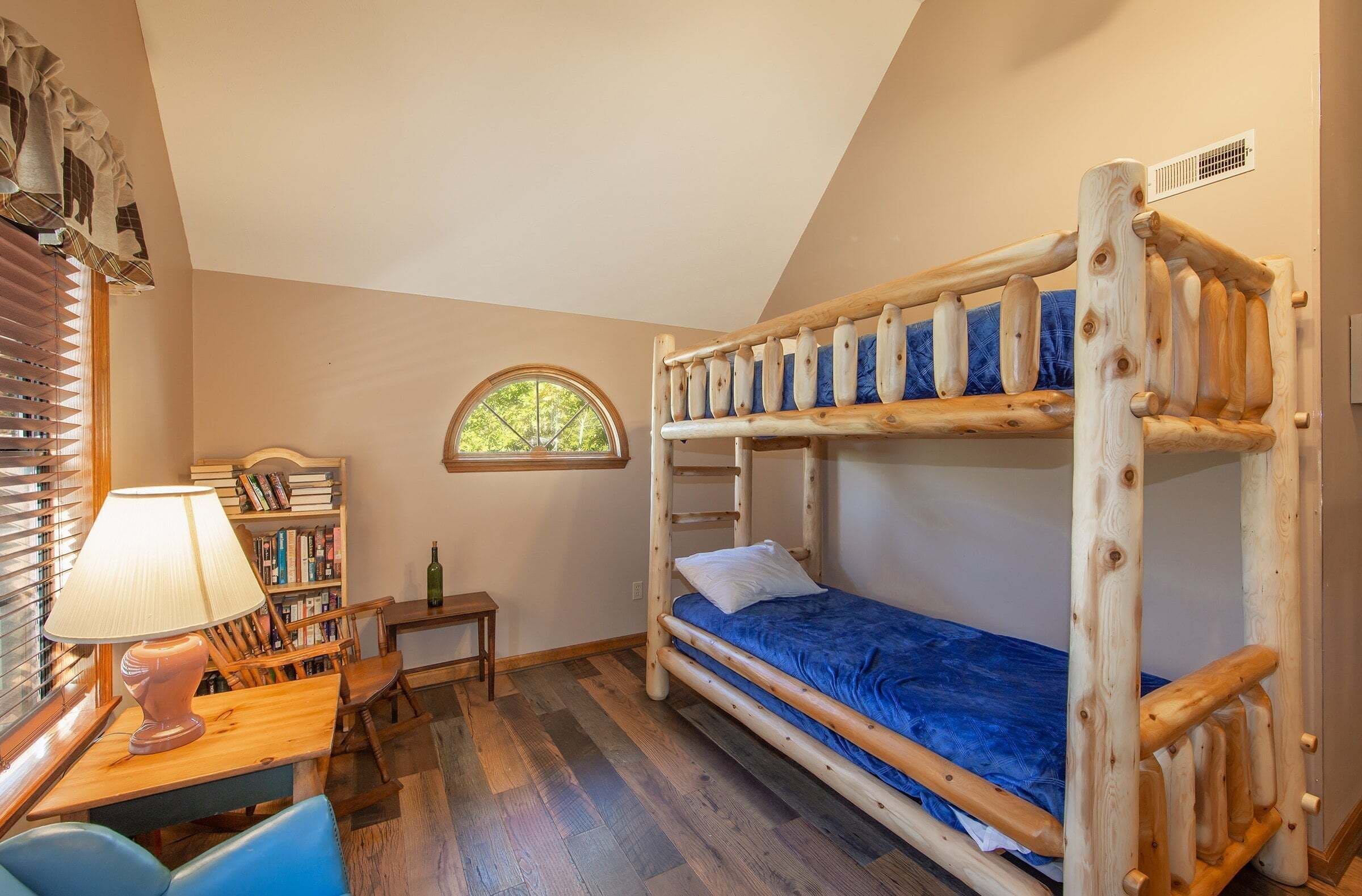 Quarto com beliche, uma janela, escrivaninha com abajur e estante de livros.