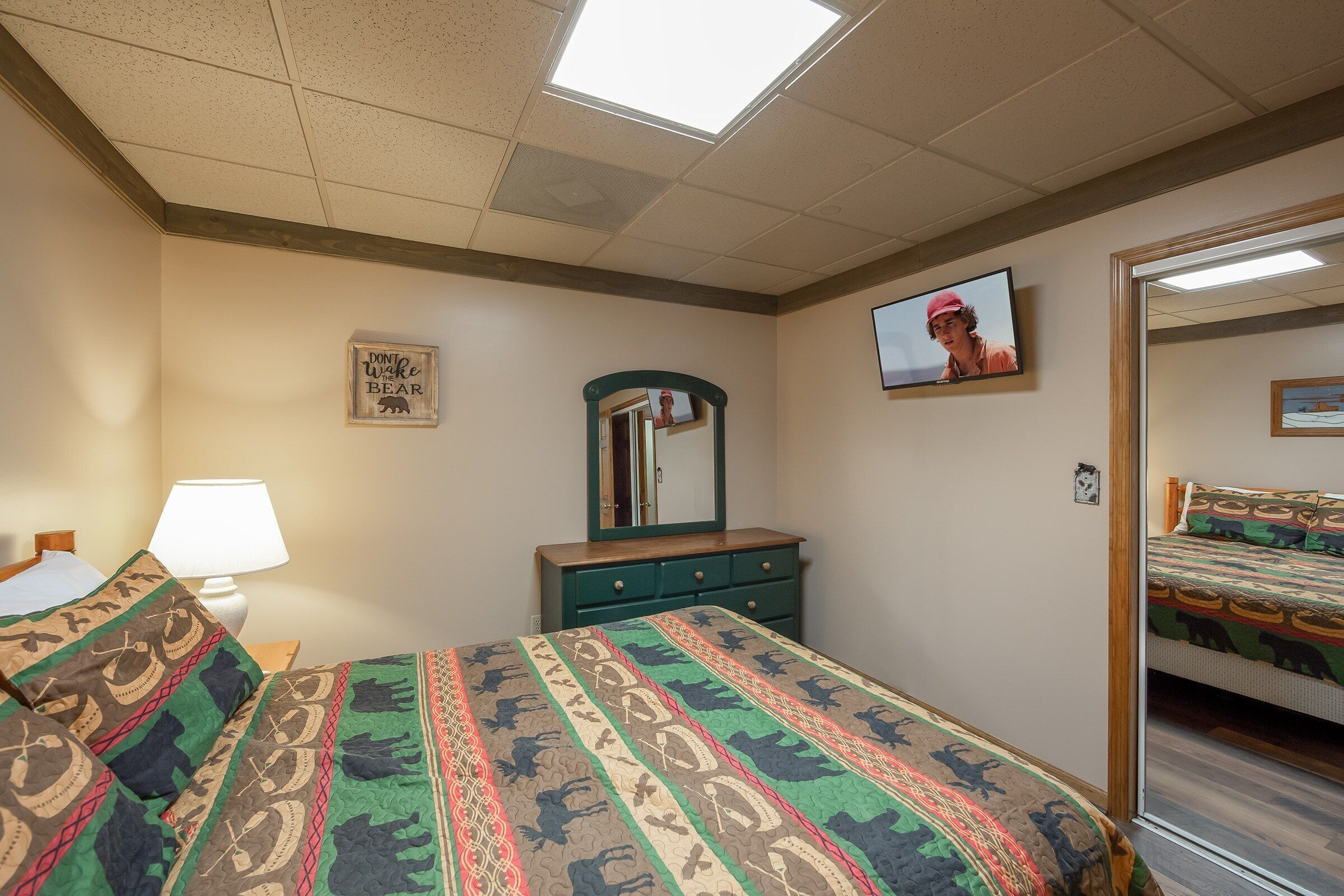 A bedroom with a bed, a dresser, a mirror, a television, and a window.