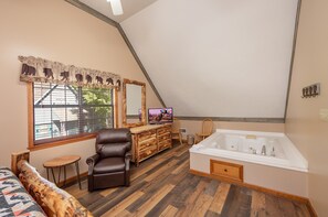 Ein Zimmer mit großem Fenster, Holzschrank, Ledersessel, Couch und einer Badewanne.