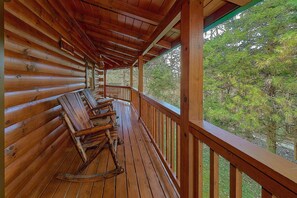 A wooden deck with a railing, wooden benches, and a view of trees. - April's Diamond Cabin Rental (Wears Valley)