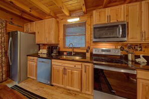 A kitchen with wooden cabinets, a stainless steel refrigerator, a dishwasher, a microwave, and an oven. - April's Diamond Cabin Rental (Wears Valley)