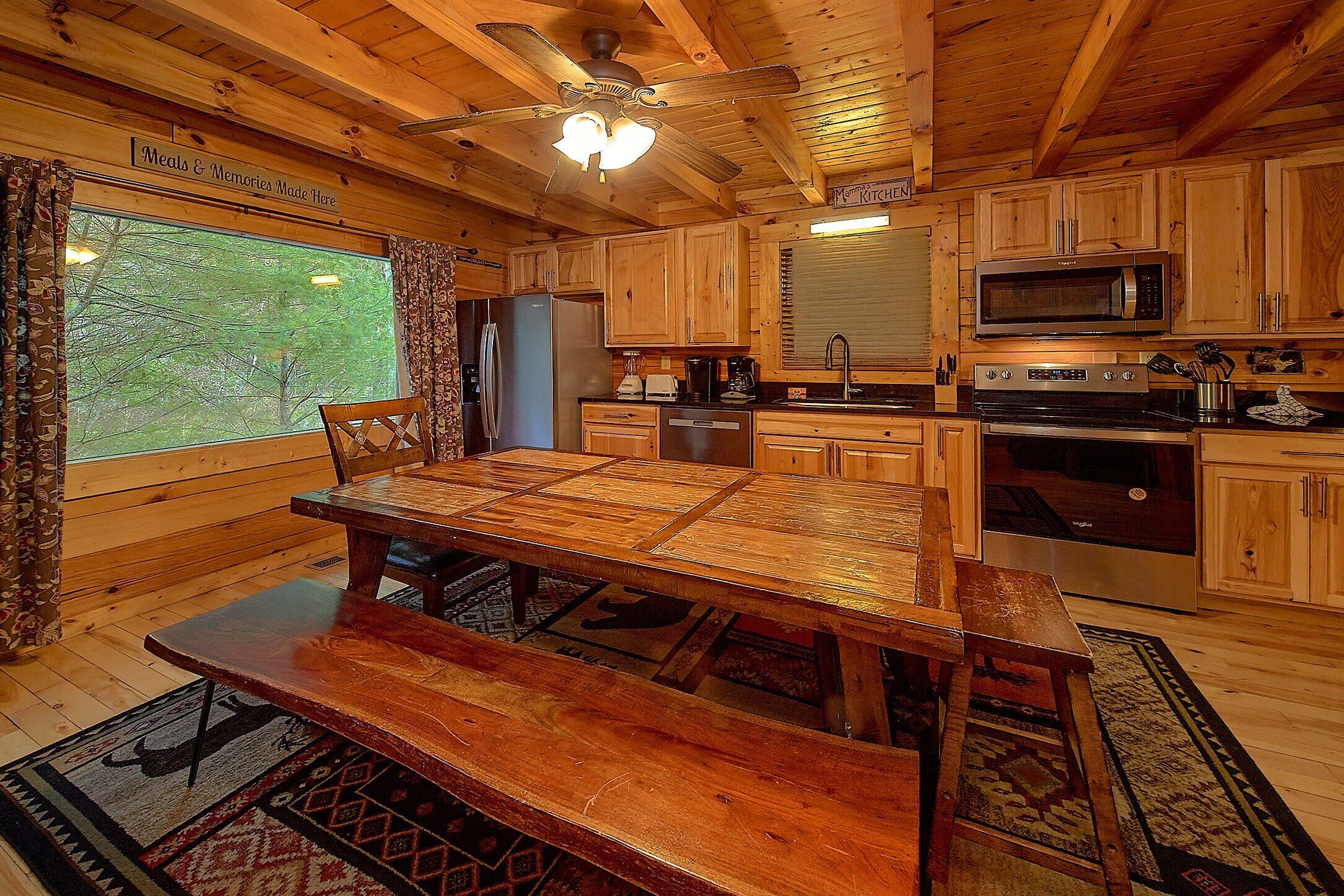 A wooden cabin interior with a dining table, kitchen area, and a view of the outdoors.