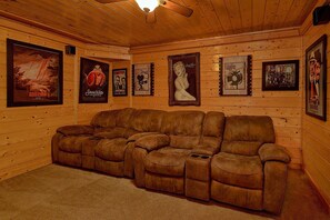 A wooden-paneled room with a reclining leather sofa and framed movie posters on the walls. - April's Diamond Cabin Rental (Wears Valley)