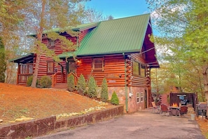 A log cabin with a green roof, a stone foundation, and a fire pit area with seating. - April's Diamond Cabin Rental (Wears Valley)