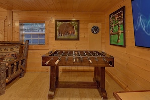 A wooden-floored room with a foosball table, a clock, and a window with blinds. - April's Diamond Cabin Rental (Wears Valley)