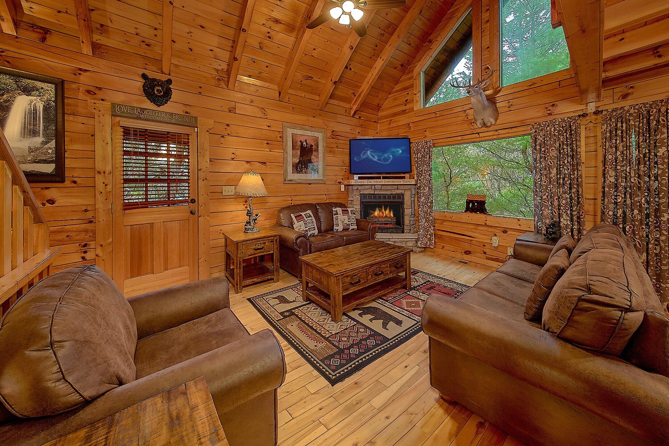 A cozy log cabin interior with a fireplace, leather sofas, a television, and a wooden ceiling.