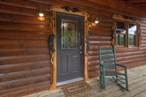 A wooden cabin with a dark front door, a welcome mat, and a green rocking chair outside. - Autumn Breeze | Hot Tub | Pool Table | Fireplace (Pigeon Forge)