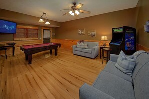 Ein Zimmer mit Billardtisch, einer Couch, einem Fernseher und einer Spielkonsole.