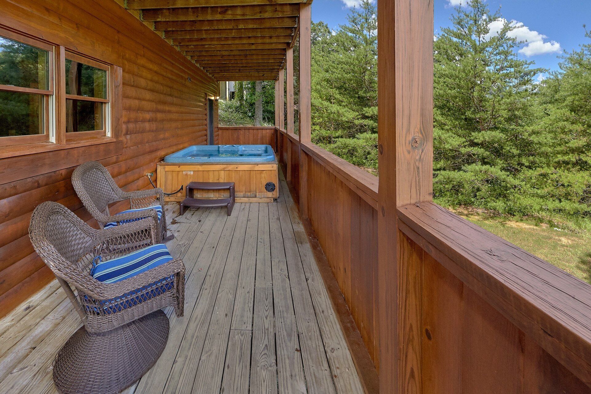 A wooden deck with a hot tub, wicker chairs, and a view of the forest.