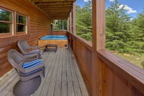 Eine Holzterrasse mit Whirlpool, Korbstühlen und Blick auf den Wald.