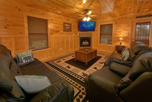 A log cabin interior with a fireplace, leather sofa, and a television mounted on the wall.