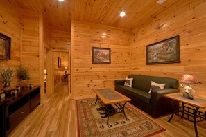A cozy log cabin interior with a sofa, a table, and a lamp. - Bear Cove Lodge Cabin Rental (Pigeon Forge)