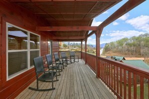 A wooden deck with a railing, several chairs, and a view of a green landscape.