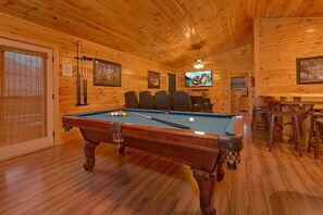 A pool table in a wooden room with a ceiling fan, a television, and a billiards rack. - Bear Cove Lodge Cabin Rental (Pigeon Forge)